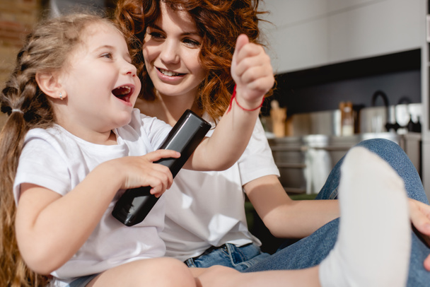 selective focus of cute kid holding remote controller near redhead mother - Foto, Imagem