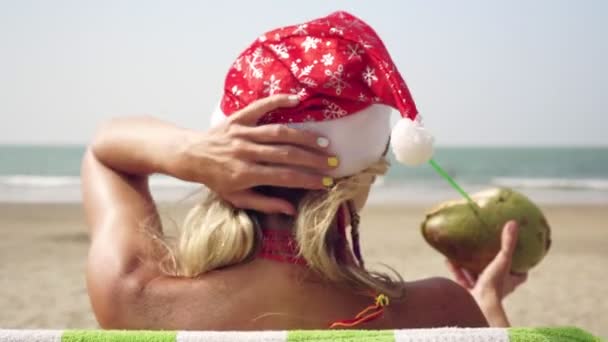 Mladá žena v klobouku Santas slaví Vánoce nebo Nový rok na tropické mořské pláži - Záběry, video