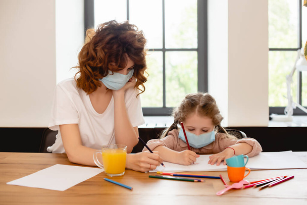 mother in medical mask drawing with daughter at home - Photo, Image