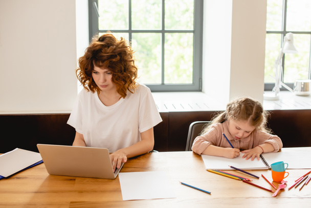 schattig dochter tekening terwijl freelancer moeder werken vanuit huis  - Foto, afbeelding