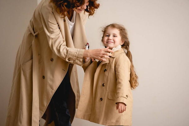happy mother touching trench coat on cheerful kid  - Foto, afbeelding