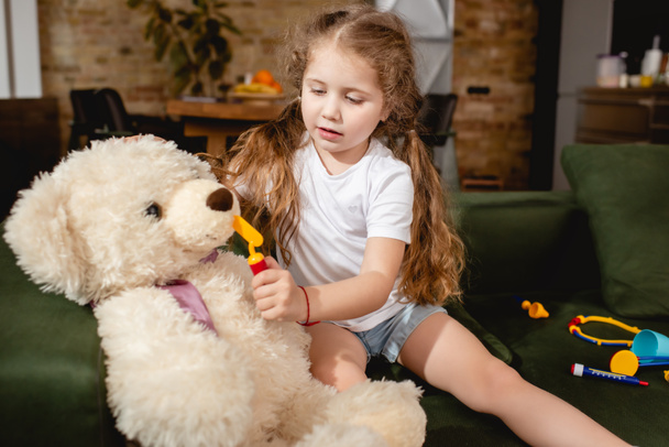 cute child holding toy near teddy bear while playing doctor game at home - Photo, Image