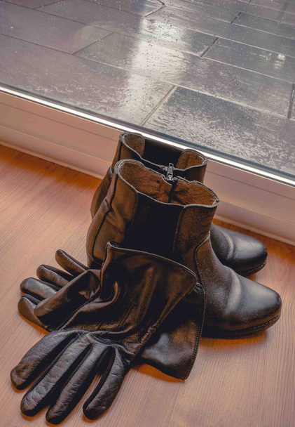 Czarne buty Chelsea i czarne rękawiczki przy oknie w deszczowy dzień. - Zdjęcie, obraz