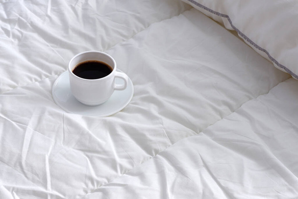 A Cup of black coffee on white bed linen. Suitable for advertising background. Minimalism. - Foto, Imagem