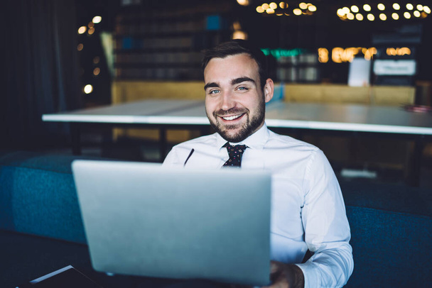 Portrait of cheerful male entrepreneur sitting in corporate workspace and smiling at camera during time for bitcoin analyzing of crypto currency exchange on trade websites, laptop investment - Foto, afbeelding