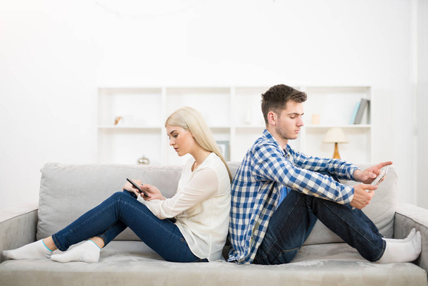 Mies ja nainen, jolla on puhelin ja tabletti, istuvat sohvalla
 - Valokuva, kuva