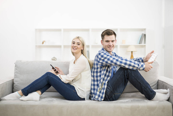 El hombre y la mujer felices con un teléfono y una tableta se sientan en el sofá
 - Foto, Imagen