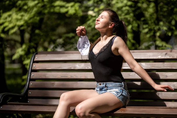 A girl sits on a bench and removes a medical mask - Photo, Image