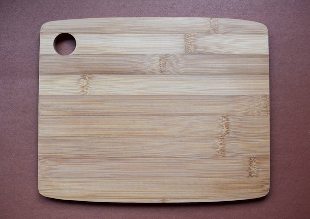 Tabla de corte de madera vacía sobre un fondo marrón
 - Foto, Imagen