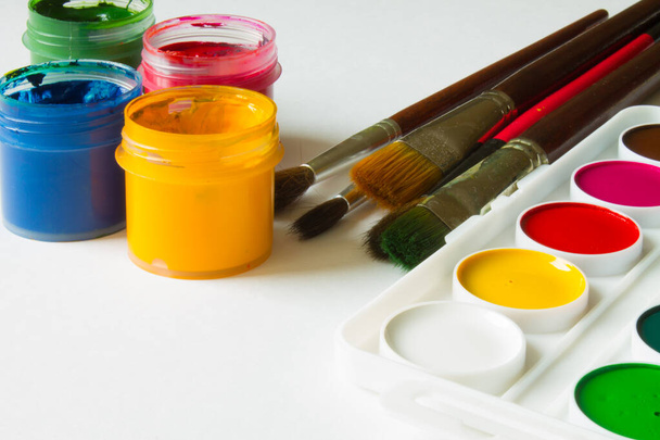 Multi-colored gouache in plastic jars, watercolor paints and art brushes on a white background close-up and copy space - Foto, imagen