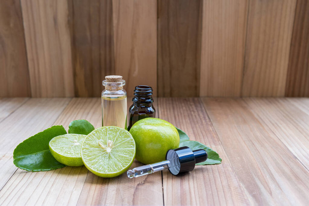 Limetten oder Zitronen ätherisches Öl Flasche mit frischen Limetten und Blättern, auf Holzbrett Hintergrund, Gesundheitskonzept. - Foto, Bild