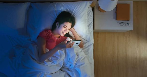Top View of asian woman use smartphone to watch video on bed at night - Foto, imagen
