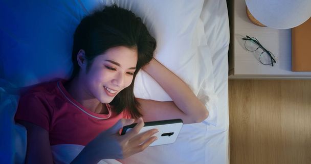 Top View of asian woman use smartphone to watch video on bed at night - Foto, Imagem