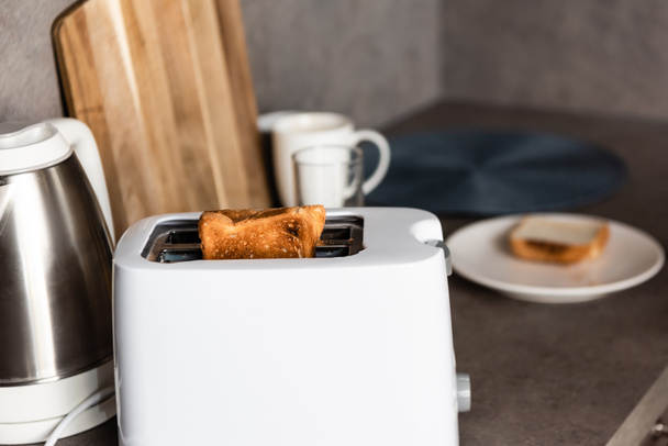 selektiver Fokus von Toaster mit Toastbrot, Wasserkocher und Schneidebrett in der Küche - Foto, Bild