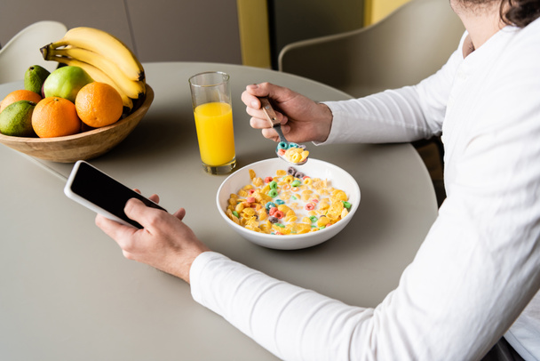 vista recortada del hombre sosteniendo el teléfono inteligente con pantalla en blanco mientras desayuna
 - Foto, Imagen