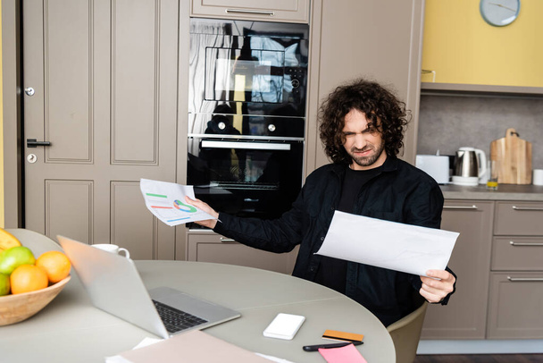 Вибірковий фокус спантеличеного фрілансера, який тримає папери біля гаджетів, кредитної картки та фруктів на кухні
  - Фото, зображення