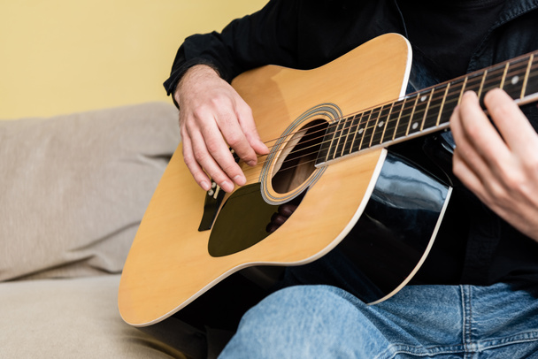 Vue recadrée de l'homme jouant de la guitare acoustique sur le canapé à la maison
  - Photo, image