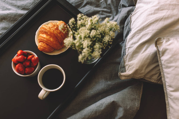 Breakfast on a tray in bed at home white dark linen. croissant tea strawberries - Φωτογραφία, εικόνα
