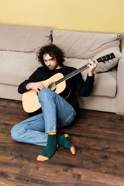 Schöner Mann performt auf Akustikgitarre auf dem Boden im Wohnzimmer - Foto, Bild