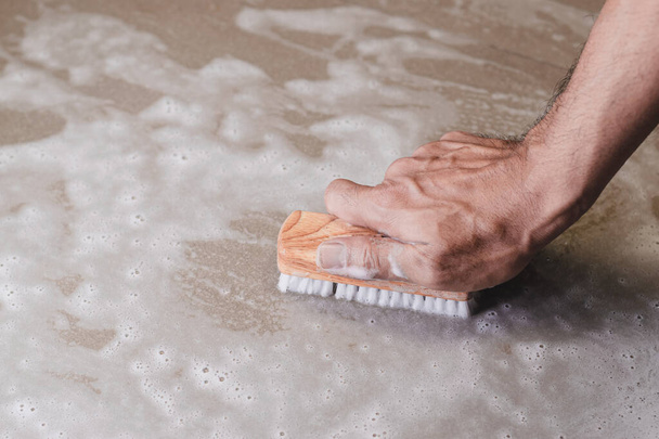 Las manos de los hombres están usando una esponja limpiando el piso de baldosas
. - Foto, Imagen