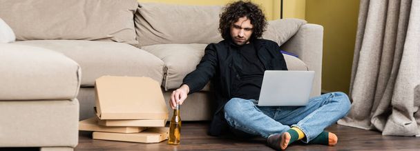 Panoráma orientációja teleworker figyelembe sörösüveg használata közben laptop közelében pizza dobozok padlón  - Fotó, kép