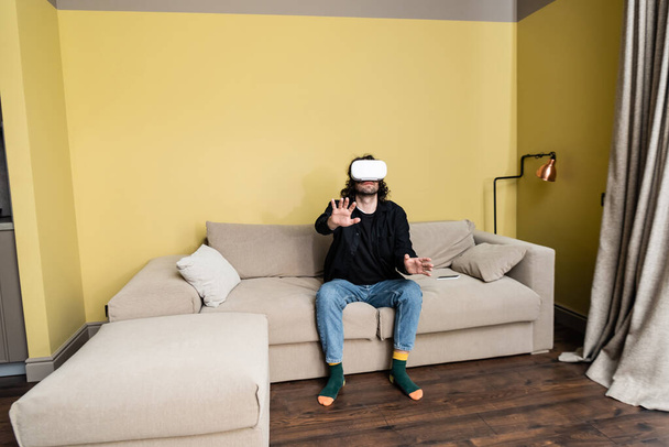 Homme bouclé jouant à un jeu vidéo en réalité virtuelle casque sur canapé
  - Photo, image