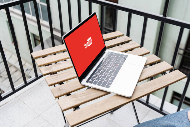 KYIV, UKRAINE - APRIL 25, 2020: Cropped view of laptop with youtube website and man sitting on balcony  - Foto, immagini