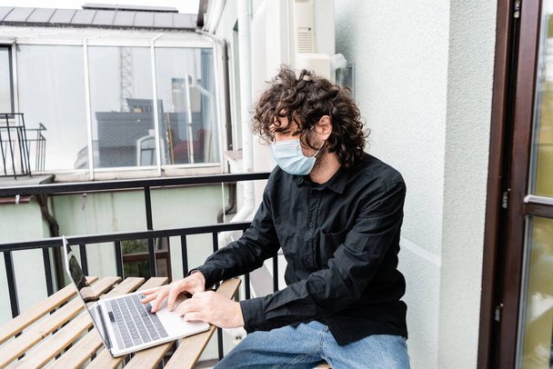 Freelancer w masce medycznej przy użyciu laptopa na balkonie w domu  - Zdjęcie, obraz