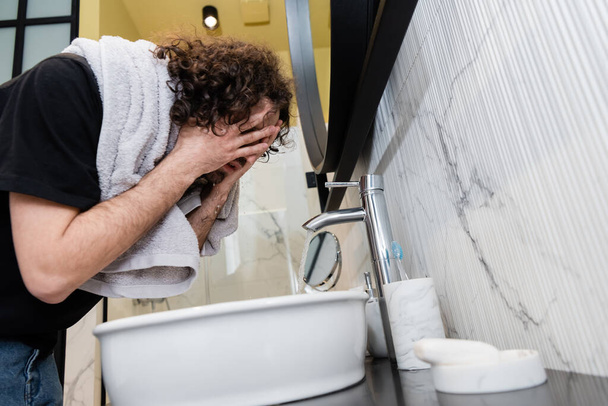 Visão de baixo ângulo do homem com toalha nos ombros lavar o rosto no banheiro
 - Foto, Imagem