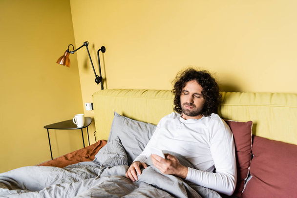 Hezký muž pomocí chytrého telefonu, zatímco sedí na posteli  - Fotografie, Obrázek