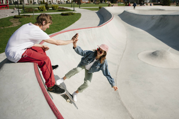 Young woman and her boyfriend spending time together in skateboard park during sunny day - Foto, Bild