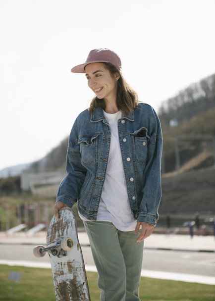 Young woman carrying skateboard looking away outdoor - Photo, Image