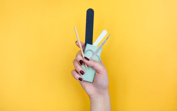 Unrecognizable female with painted nails showing bunch of various manicure tools against bright yellow background - Фото, зображення