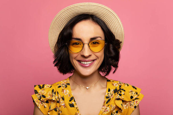 Sunny girl. Close-up photo of a lovely young girl in a yellow dress, yellow sunglasses and straw hat, who is looking in the camera with a big smile. - Foto, Imagen