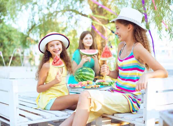 Счастливые друзья на пикнике едят арбуз и улыбаются друг другу в солнечный день. Девочки-подростки веселятся вместе. Концепция летнего времени
 - Фото, изображение