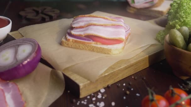 haciendo el sándwich con bacon en rodajas en vinagre y verduras en la tabla de madera
 - Imágenes, Vídeo