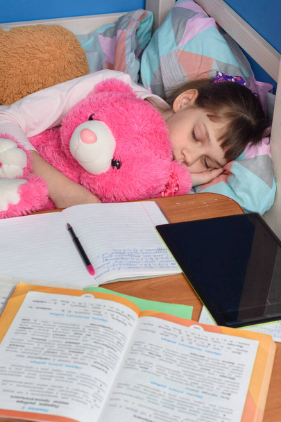 Girl fell asleep in a hug with a teddy bear doing lessons at home - Photo, Image