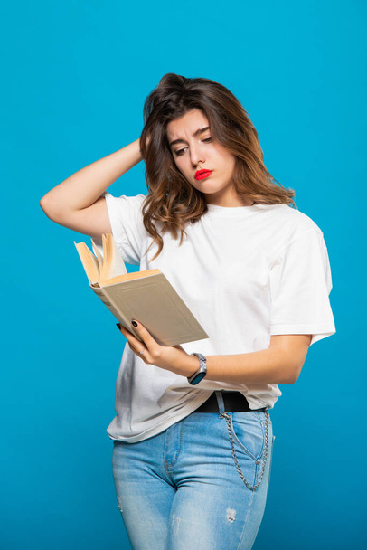 Young pretty female student is reading a book. Woman Isolated on a blue background. On the girl a t-shirt and jeans. - Foto, Imagem