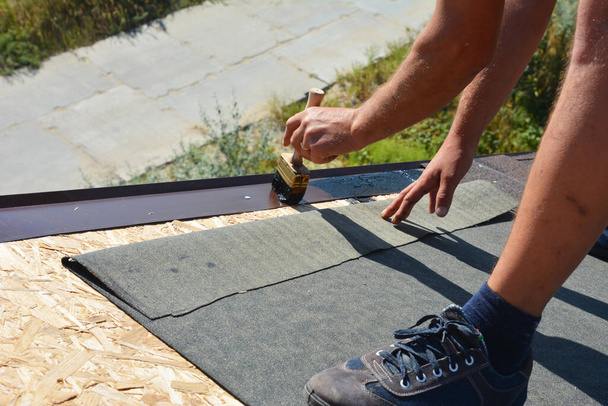 A building contractor is installing underlayment, a layer of bitumen tape on sheathing for overall roof protection at the ridge of the rooftop on the house construction, repairing. - Photo, Image