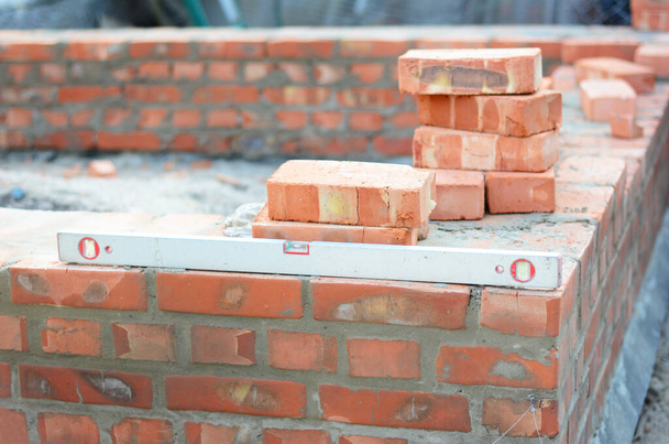 Bau einer Ziegelmauerecke einer Hauskonstruktion mit Wasserwaage, um das Mauerwerk aufrecht und eben auf einem Mörtelbett zu halten. - Foto, Bild