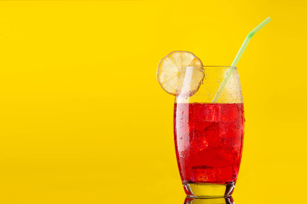 glass of soft drink with a lot of ice a slice of lemon and a straw on yellow background - Photo, Image