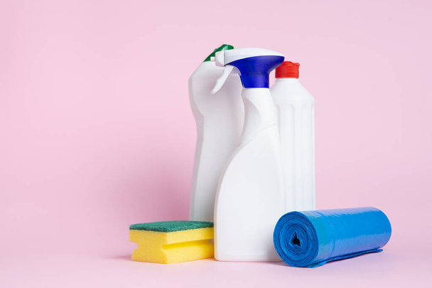 Drei Dosen Reinigungsmittel sprühen mit einem Scheuersauger und Müllsäcken auf rosa Hintergrund - Foto, Bild