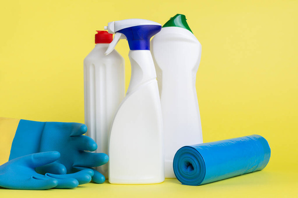 Drei Dosen Reinigungsspray mit Scheuerpad, Kugeln und Müllsäcken auf gelbem Hintergrund - Foto, Bild