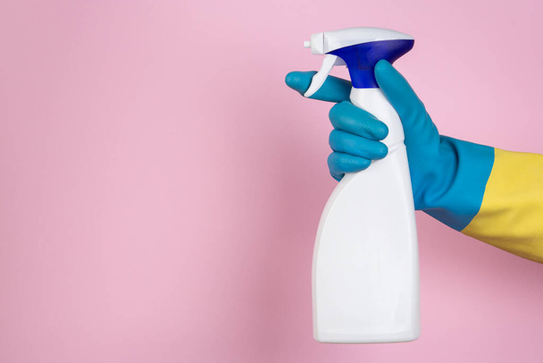 Una mano con guantes de limpieza apretando una botella de spray sobre un fondo rosa
 - Foto, imagen