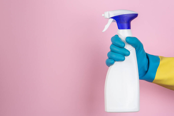 A hand with cleaning gloves squeezing a spray bottle on a pink background - Foto, Imagem