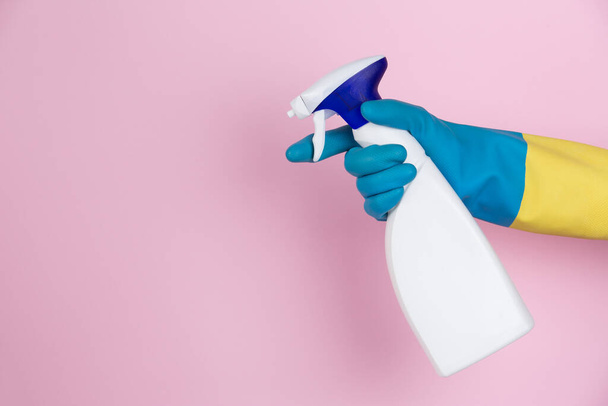 Uma mão com luvas de limpeza apertando uma garrafa de spray em um fundo rosa
 - Foto, Imagem