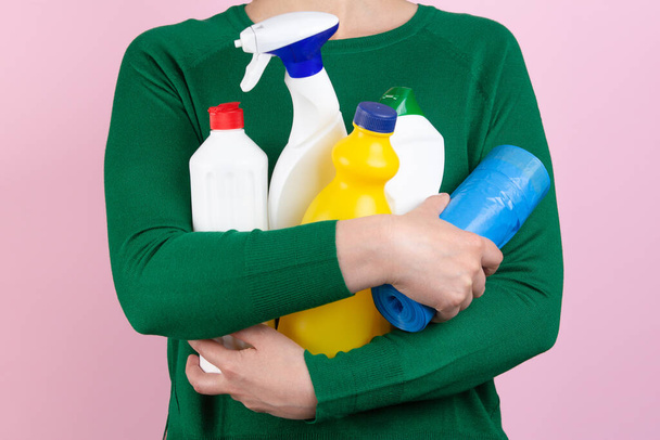 femme avec pull vert et fond rose étreignant de nombreux produits de nettoyage dans ses bras
 - Photo, image