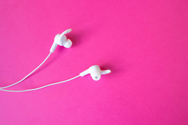 Casques d'écoute blancs avec fil sur fond rose. Le concept de gadgets. - Photo, image