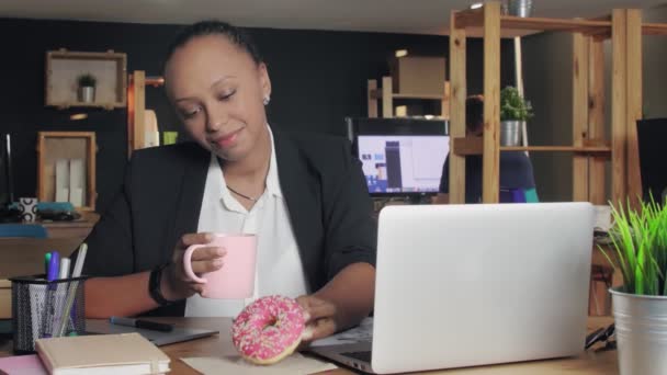 Young african american woman having lunch at office. Woman dont want eats a donut, she decided to eats vegetables - Séquence, vidéo