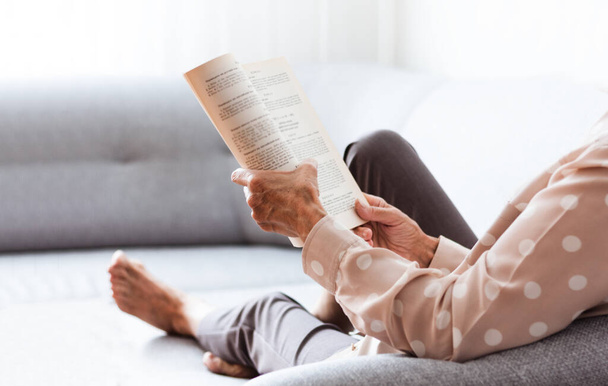 Middle-aged brunette woman on the gray sofa reading book, soft focus, stay at home concept, cozy background - Photo, Image